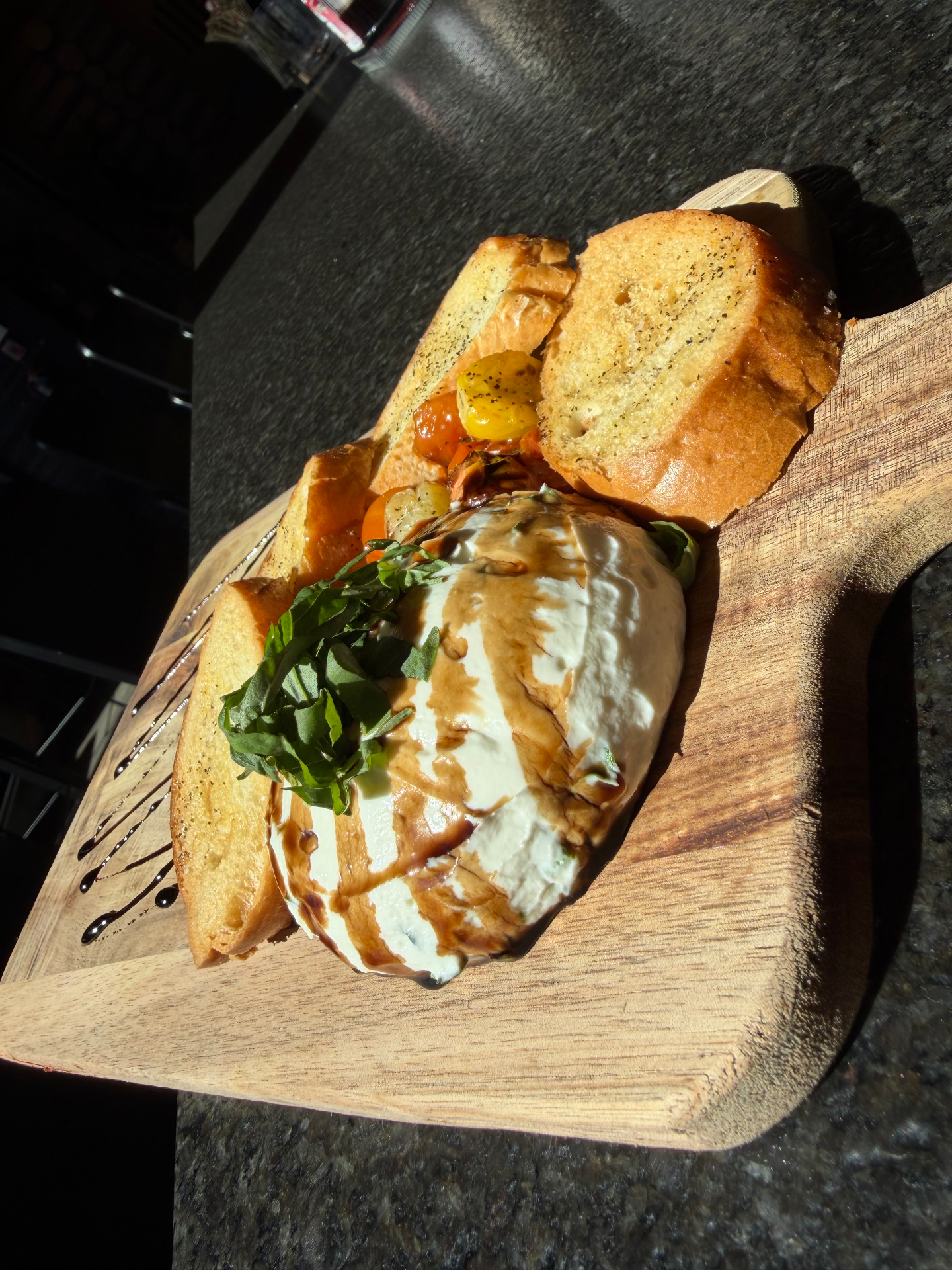 Burrata with toasted bread, tomatoes, basil, and balsamic on a wooden board by Zach Lucchetti